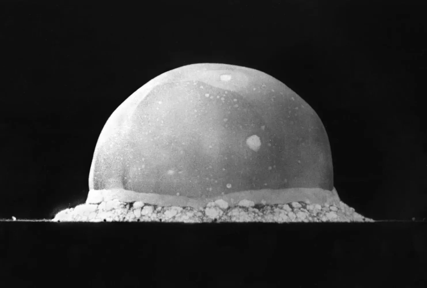 A black and white photograph of a dome of fire at ground level, moments after the first nuclear test.