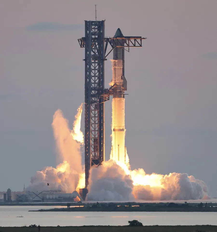 A very tall rocket on a launch tower with bright flames at its base.