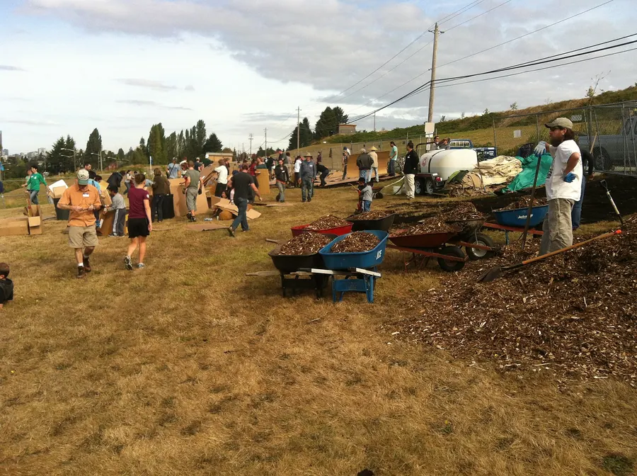 People with wheelbarrows on a bare mulched site where a public food forest is being built.